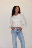 Woman wearing a white lace top and blue jeans against a plain background