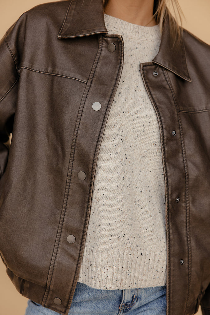 Brown leather jacket over a light-colored sweater and jeans on a neutral background