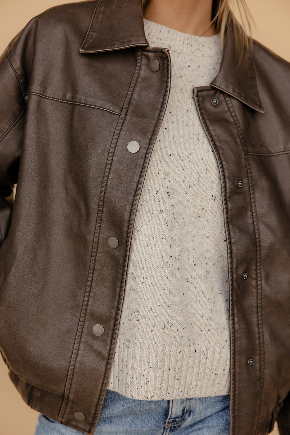 Brown leather jacket over a light-colored sweater and jeans on a neutral background