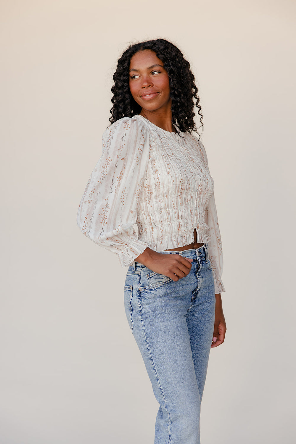 Woman wearing a white lace top and blue jeans against a plain background
