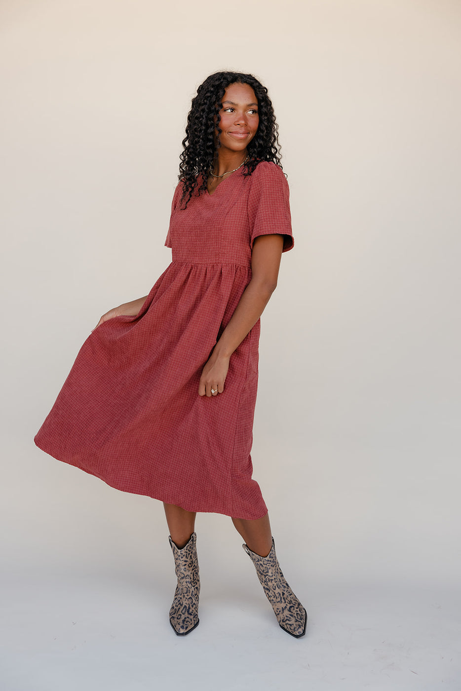 Woman wearing a red dress with short sleeves and a skirt on a plain background