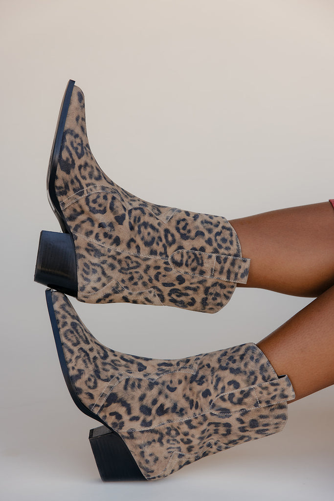 Leopard print boots worn by a person on a plain background