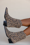 Leopard print boots worn by a person on a plain background