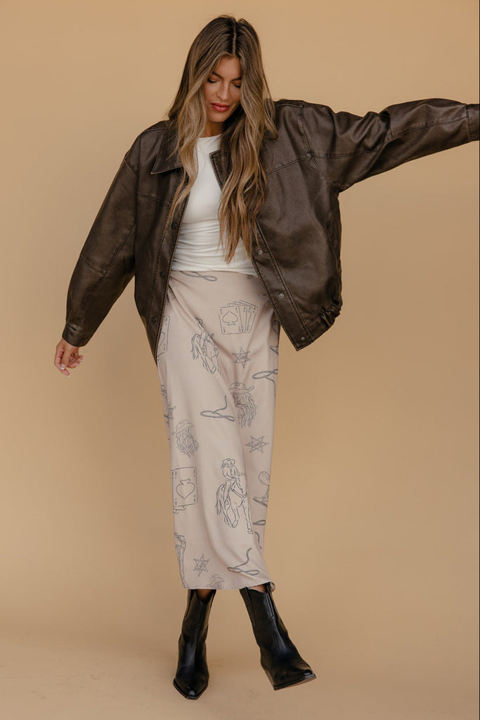 Woman wearing a brown jacket, white top, and patterned pants on a beige background