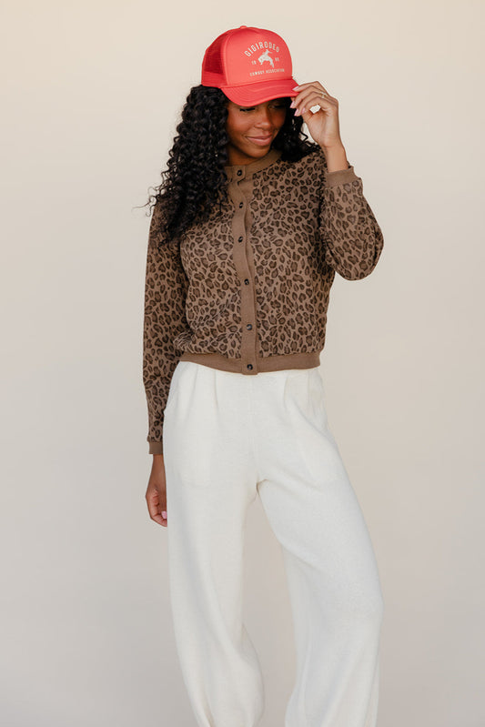Person wearing a red cap and leopard print top with white pants on a beige background