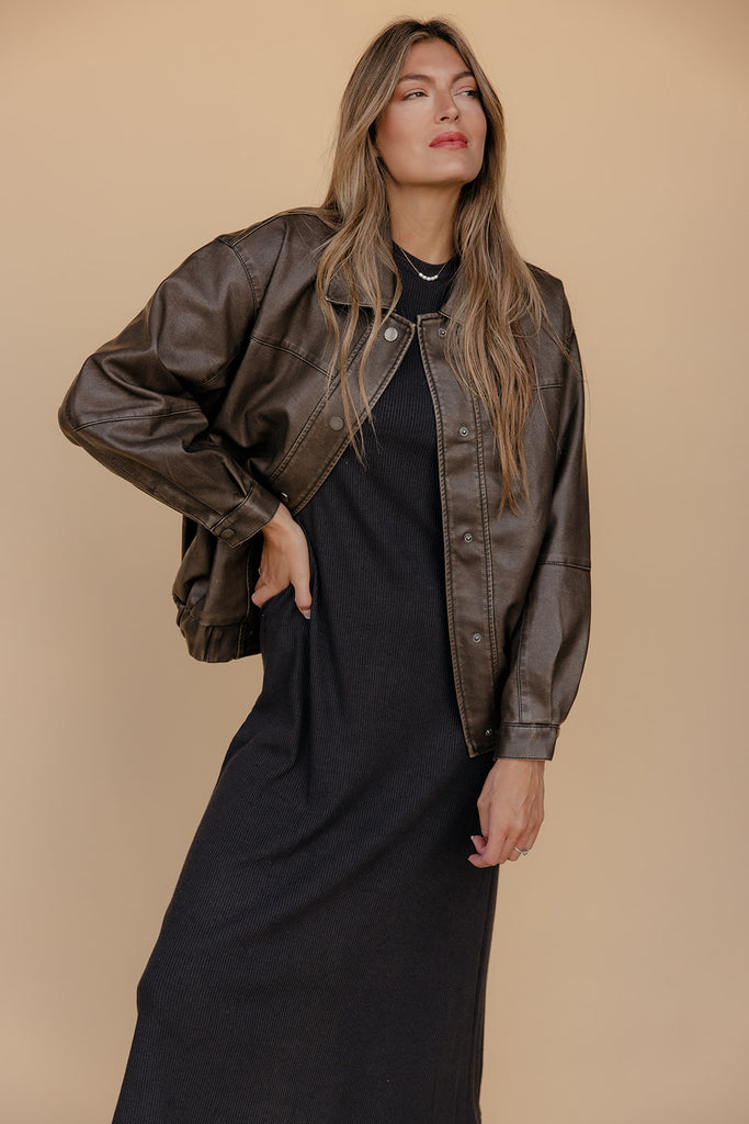 Woman wearing a black dress and brown leather jacket against a beige background