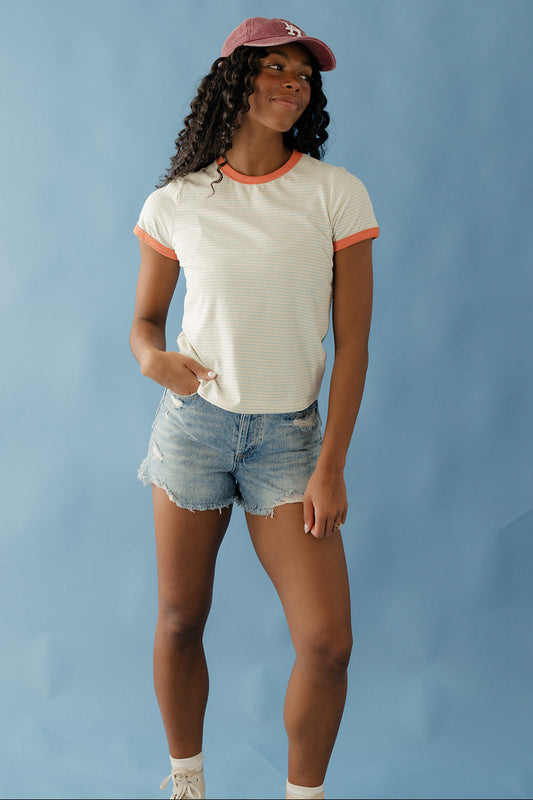 Woman wearing a white t-shirt with orange trim and denim shorts against a blue background