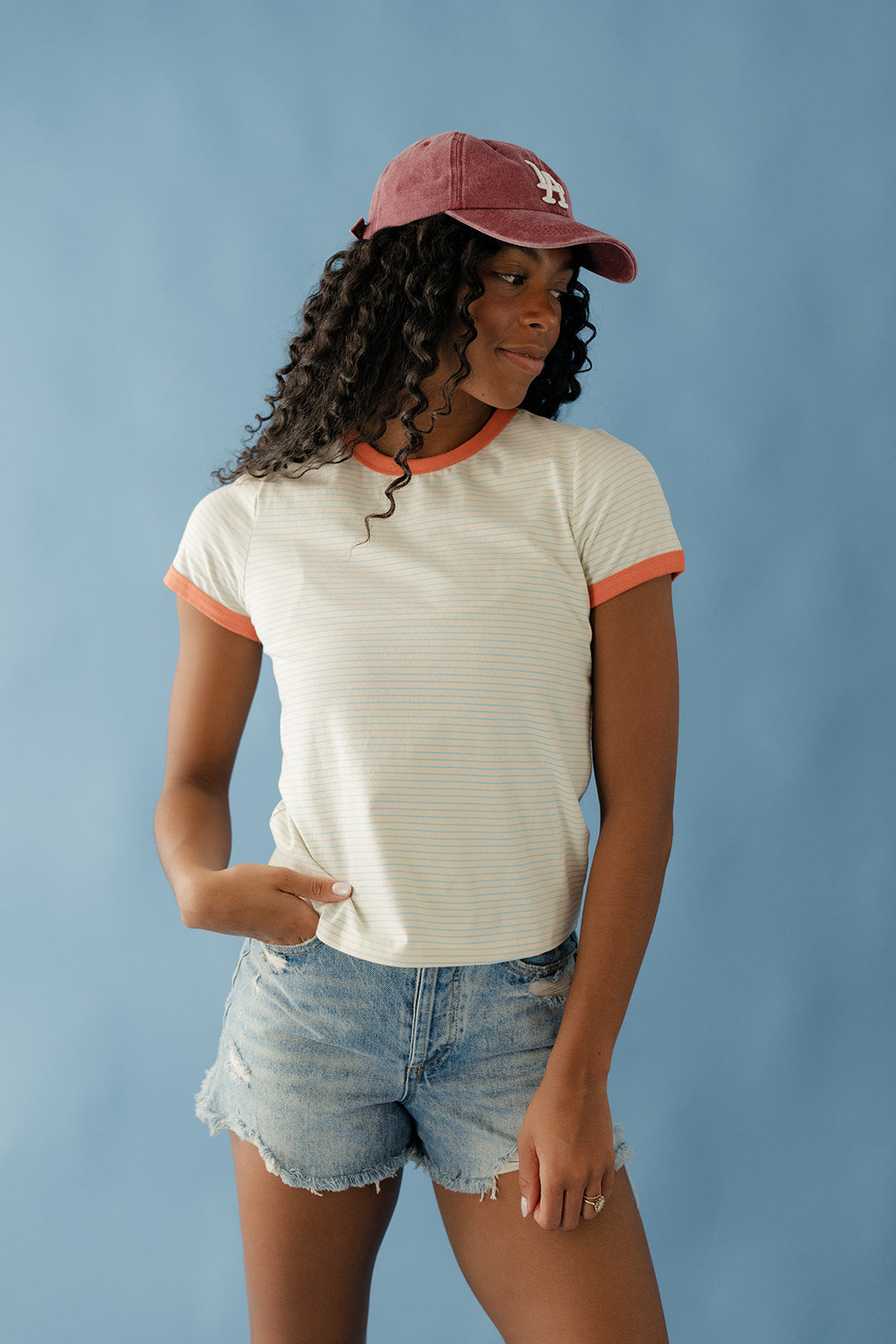 Woman wearing a white t-shirt with orange trim and denim shorts against a blue background