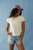 Woman wearing a white t-shirt with orange trim and denim shorts against a blue background