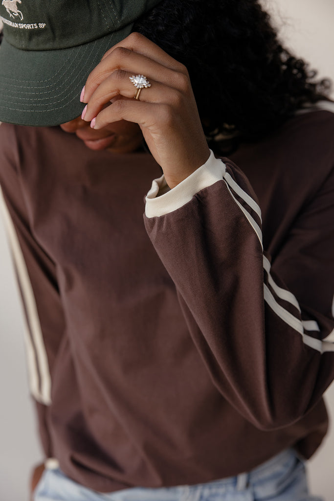 Person wearing a brown jacket with white stripes and a green cap, holding a phone.