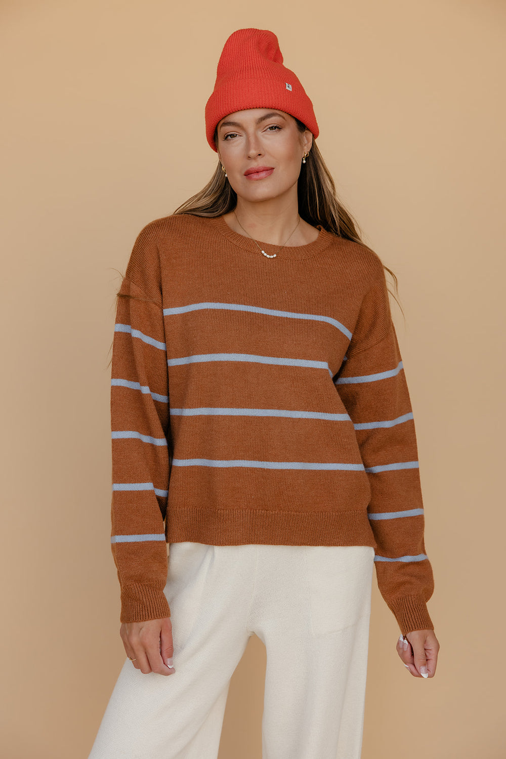 Woman wearing a brown striped sweater and red beanie against a beige background