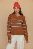Woman wearing a brown striped sweater and red beanie against a beige background