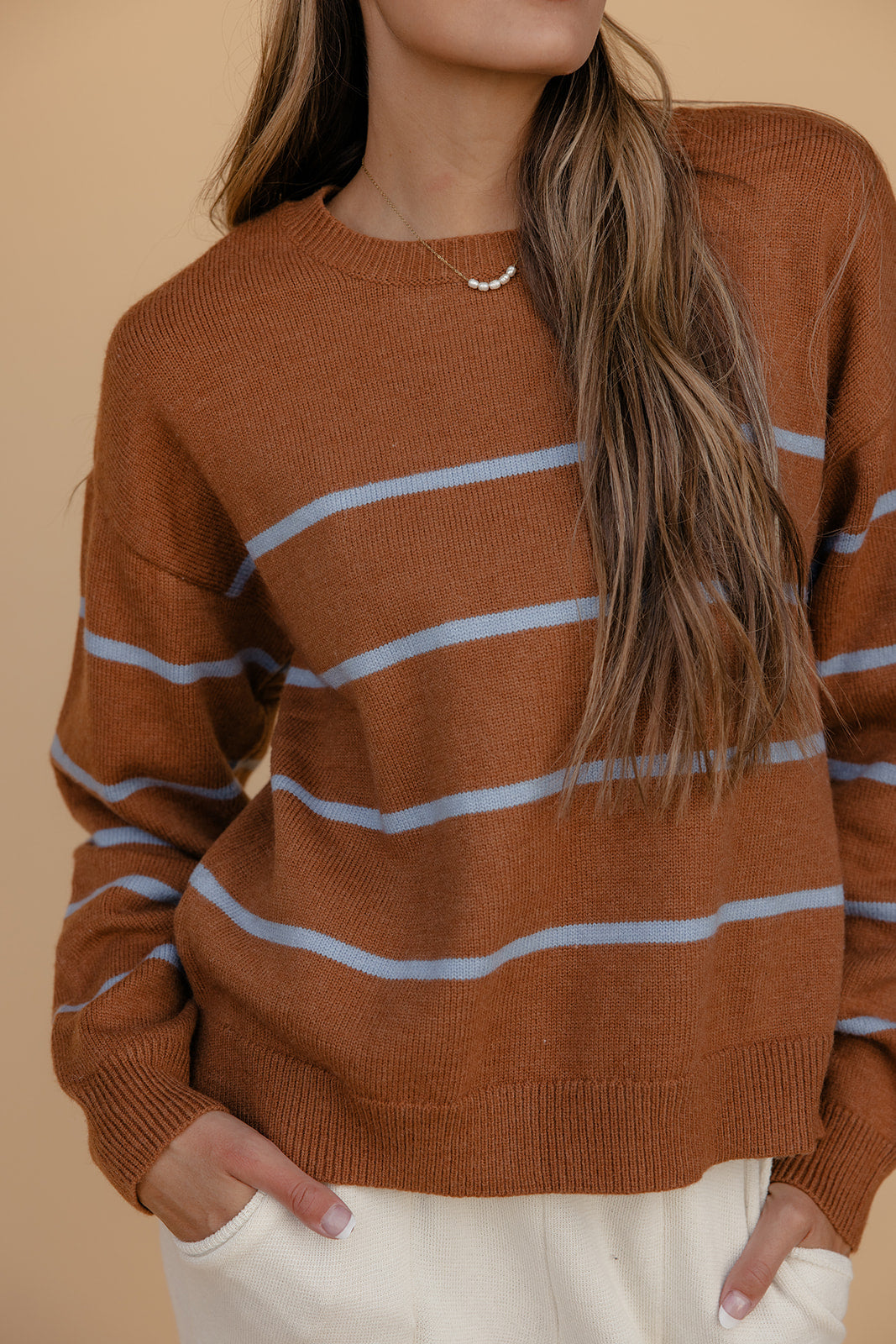 Person wearing a brown sweater with blue stripes against a beige background