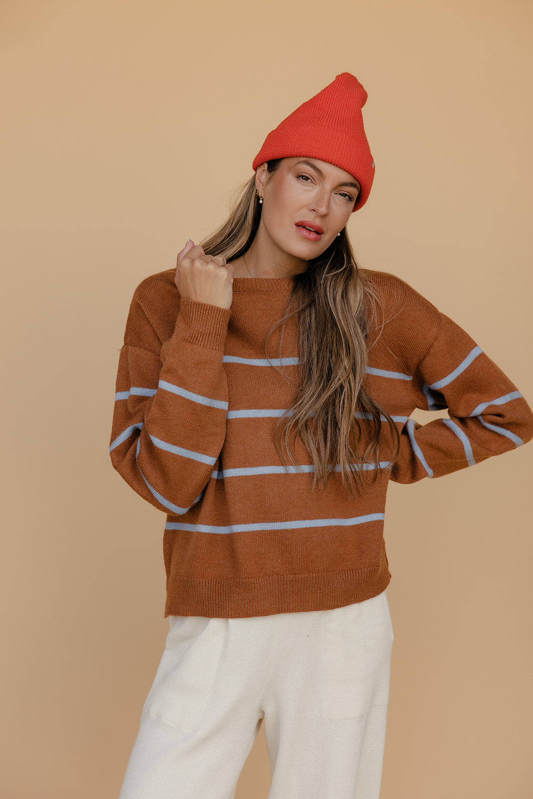 Woman wearing a brown striped sweater and red beanie against a beige background