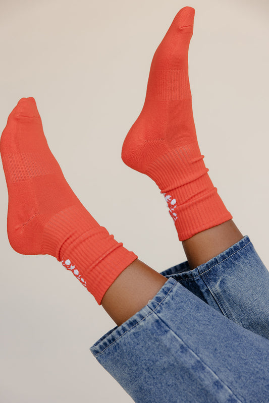 Orange socks with white text worn with blue jeans on a beige background
