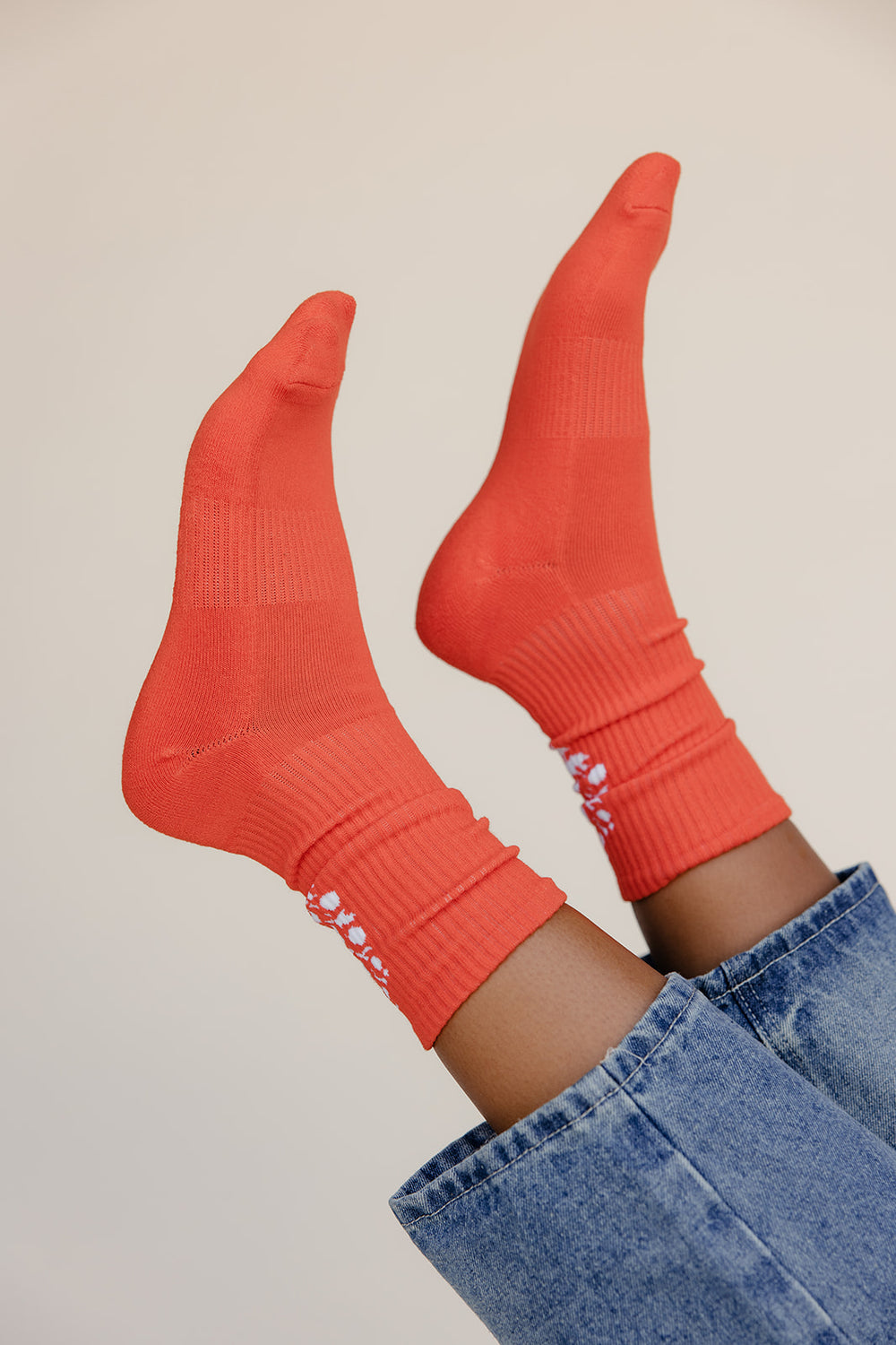 Red socks with white text worn with blue jeans on a neutral background