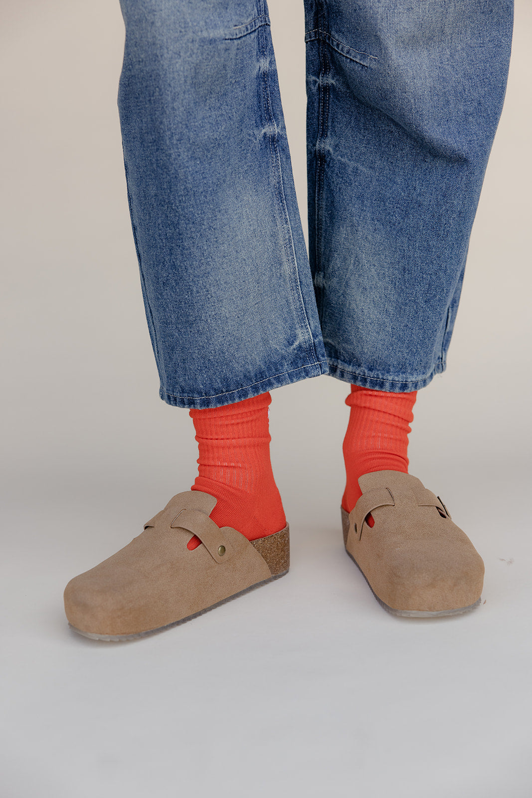 Person wearing blue jeans, red socks, and brown shoes on a plain background