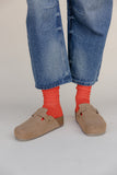 Person wearing blue jeans, red socks, and brown shoes on a plain background