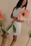 Woman in a polka dot dress holding large pink flowers against a beige background