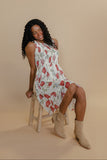 Woman sitting on a stool wearing a floral dress and beige boots against a beige background