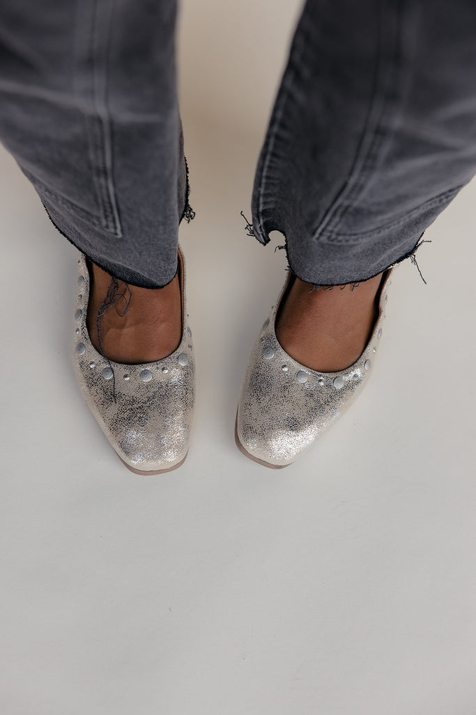 Silver glittery flats worn with gray jeans on a plain background