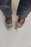 Silver glittery flats worn with gray jeans on a plain background