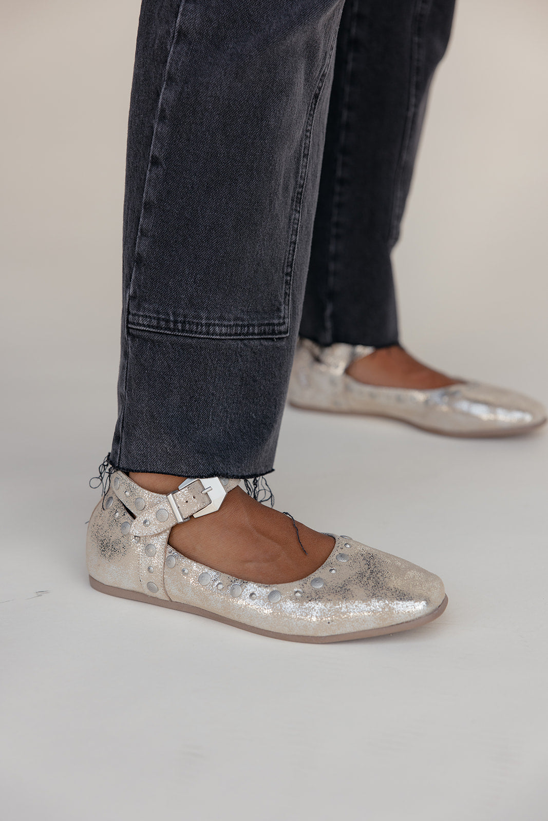 Silver glittery flats worn with dark jeans on a plain background