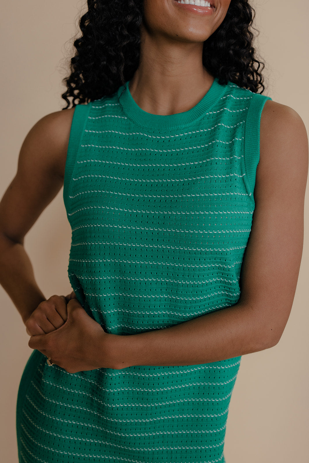 Woman wearing a green sleeveless dress with white stripes against a beige background