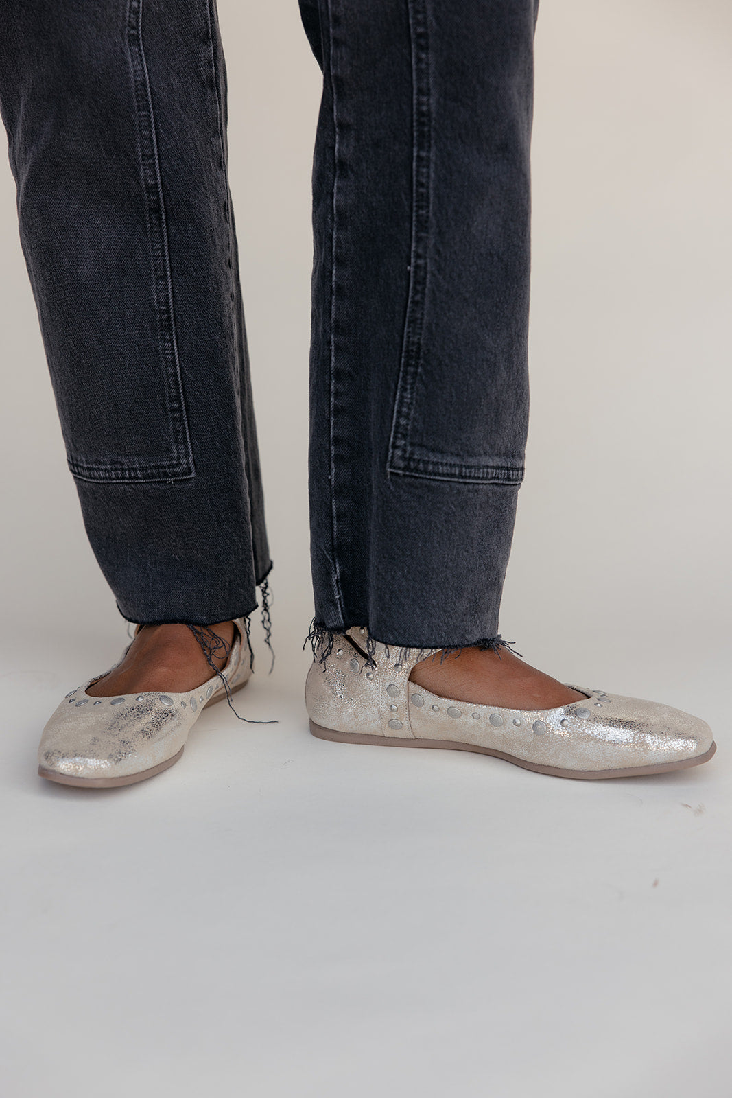 Person wearing dark jeans and metallic loafers on a plain background