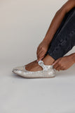 Person putting on a silver glittery shoe with a plain background