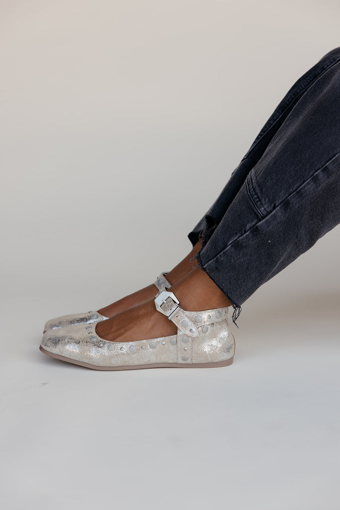 Silver glittery flats worn with dark jeans on a plain background