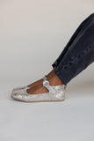 Silver glittery flats worn with dark jeans on a plain background