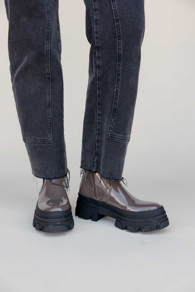 Transparent rain boots with black soles worn with dark jeans on a white background