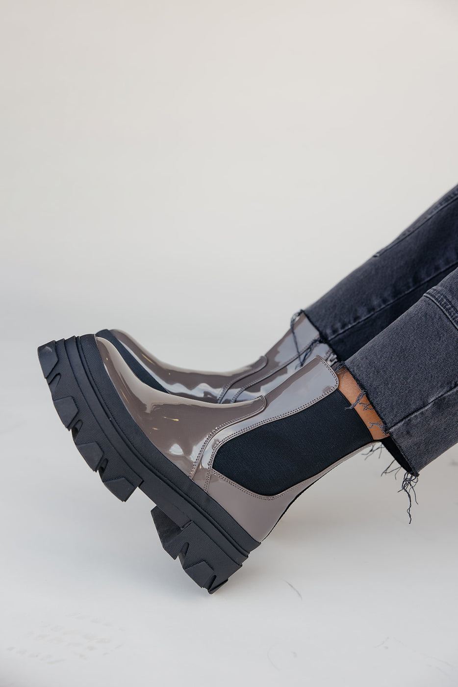 Black and transparent rain boots worn with jeans on a light gray background