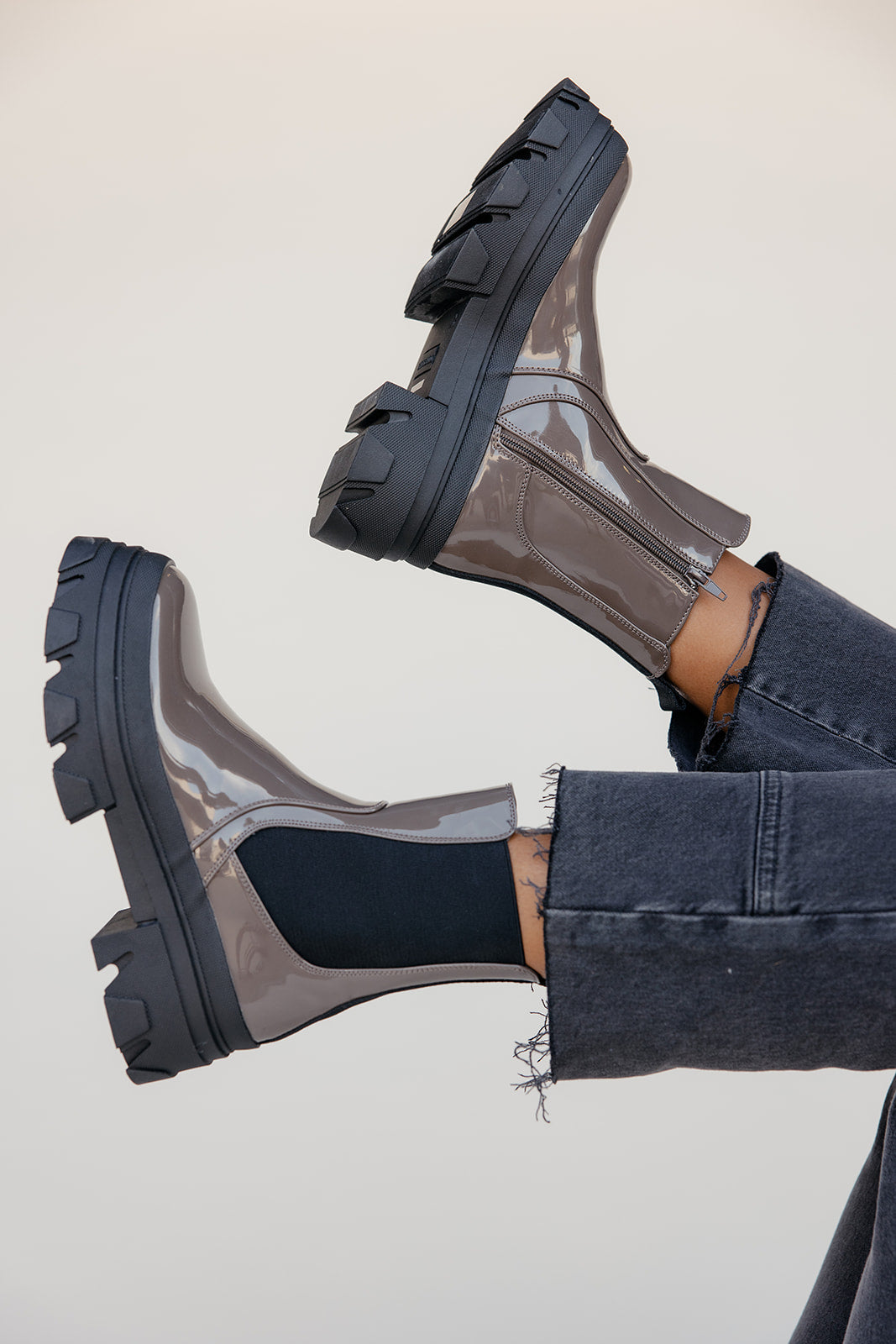 Clear rain boots with black soles worn by a person on a light background