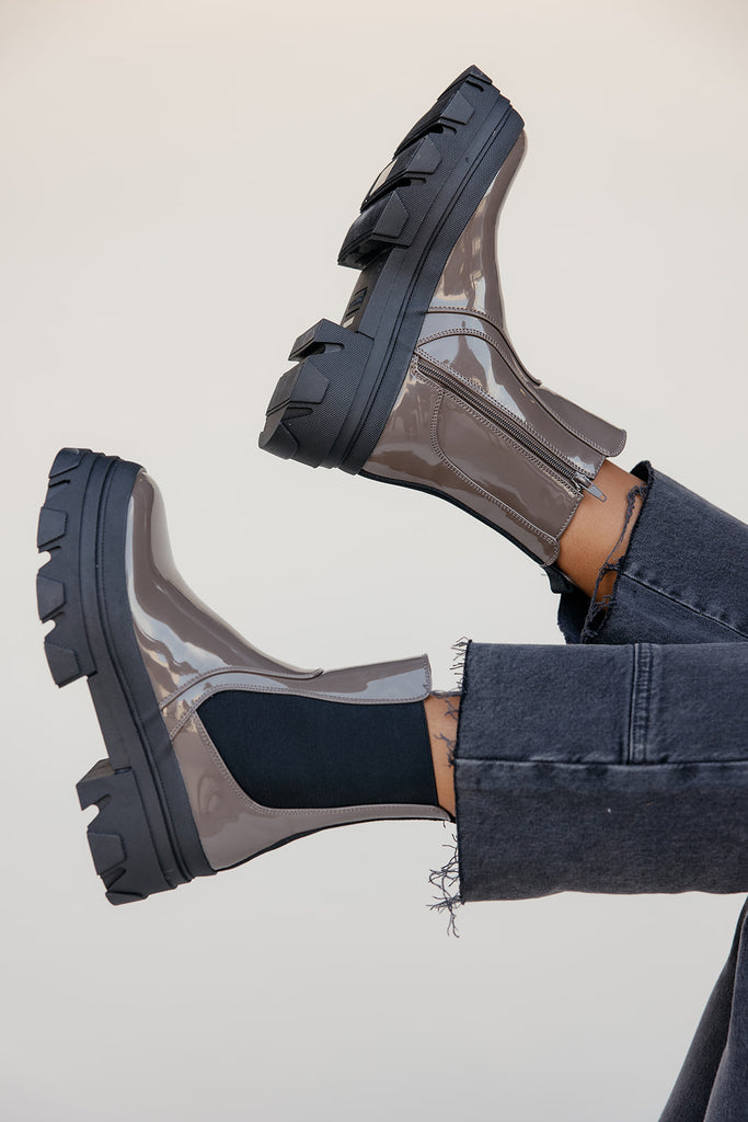 Clear rain boots with black soles worn by a person on a light background