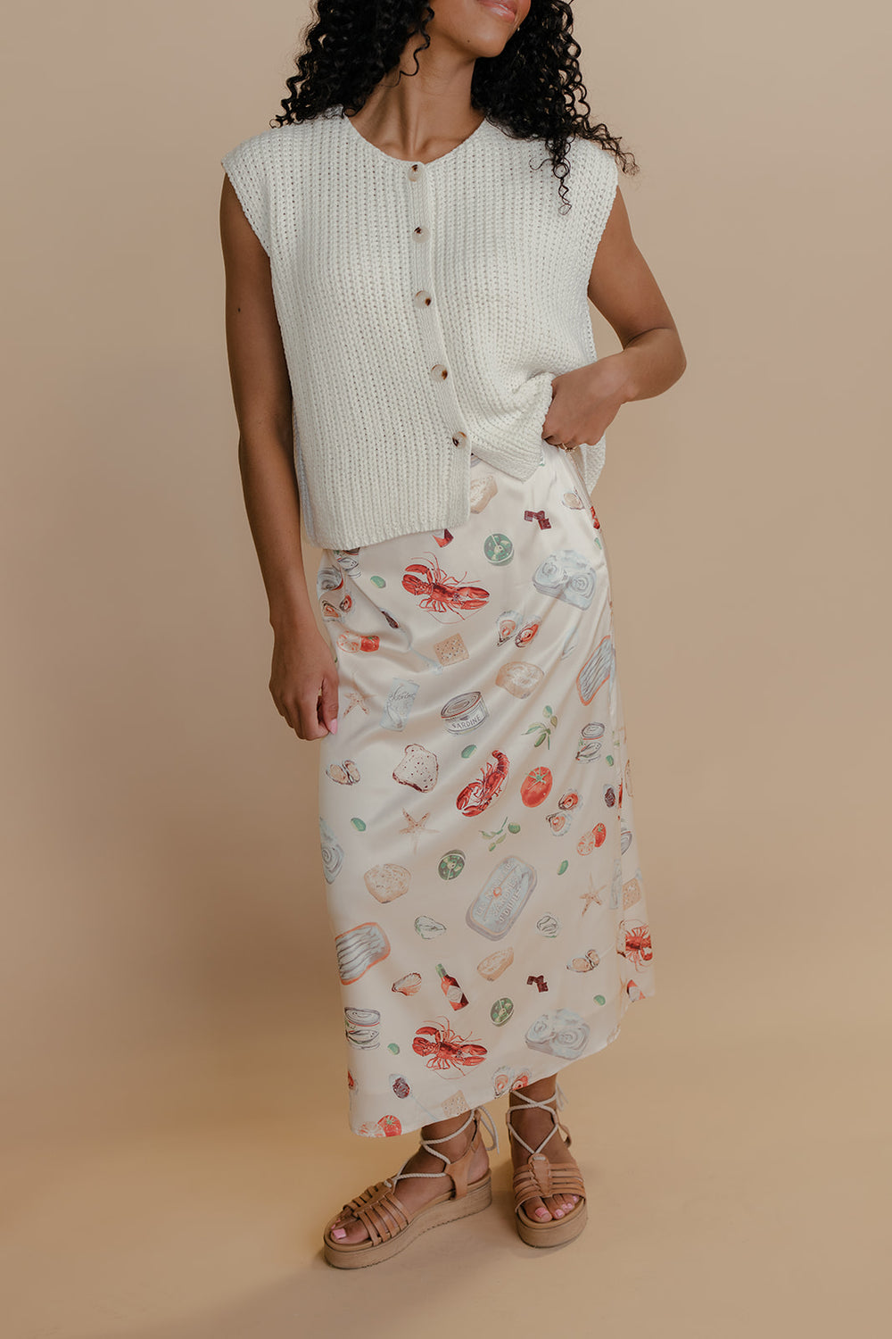 Woman wearing a white sleeveless top and patterned skirt against a beige background