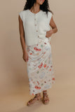Woman wearing a white sleeveless top and patterned skirt against a beige background