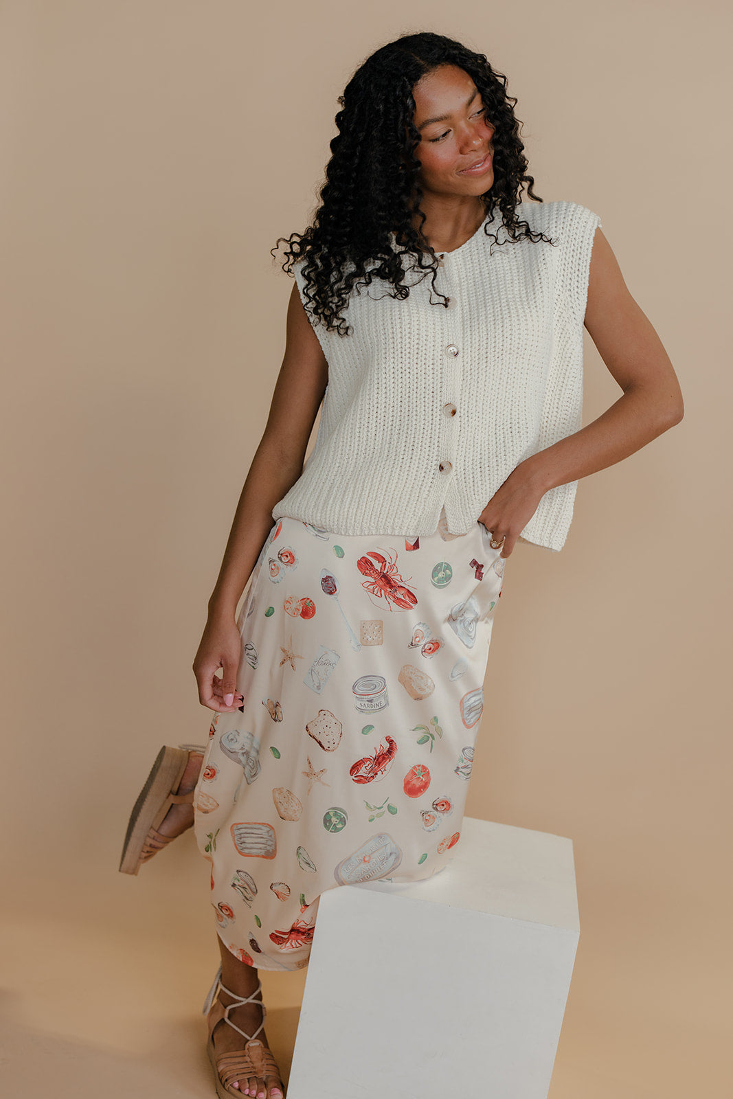 Woman wearing a sleeveless knit top and patterned pants against a beige background