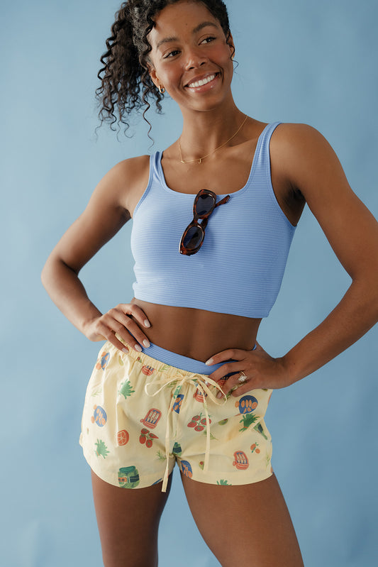 Woman wearing a blue sports bra and patterned shorts against a light blue background