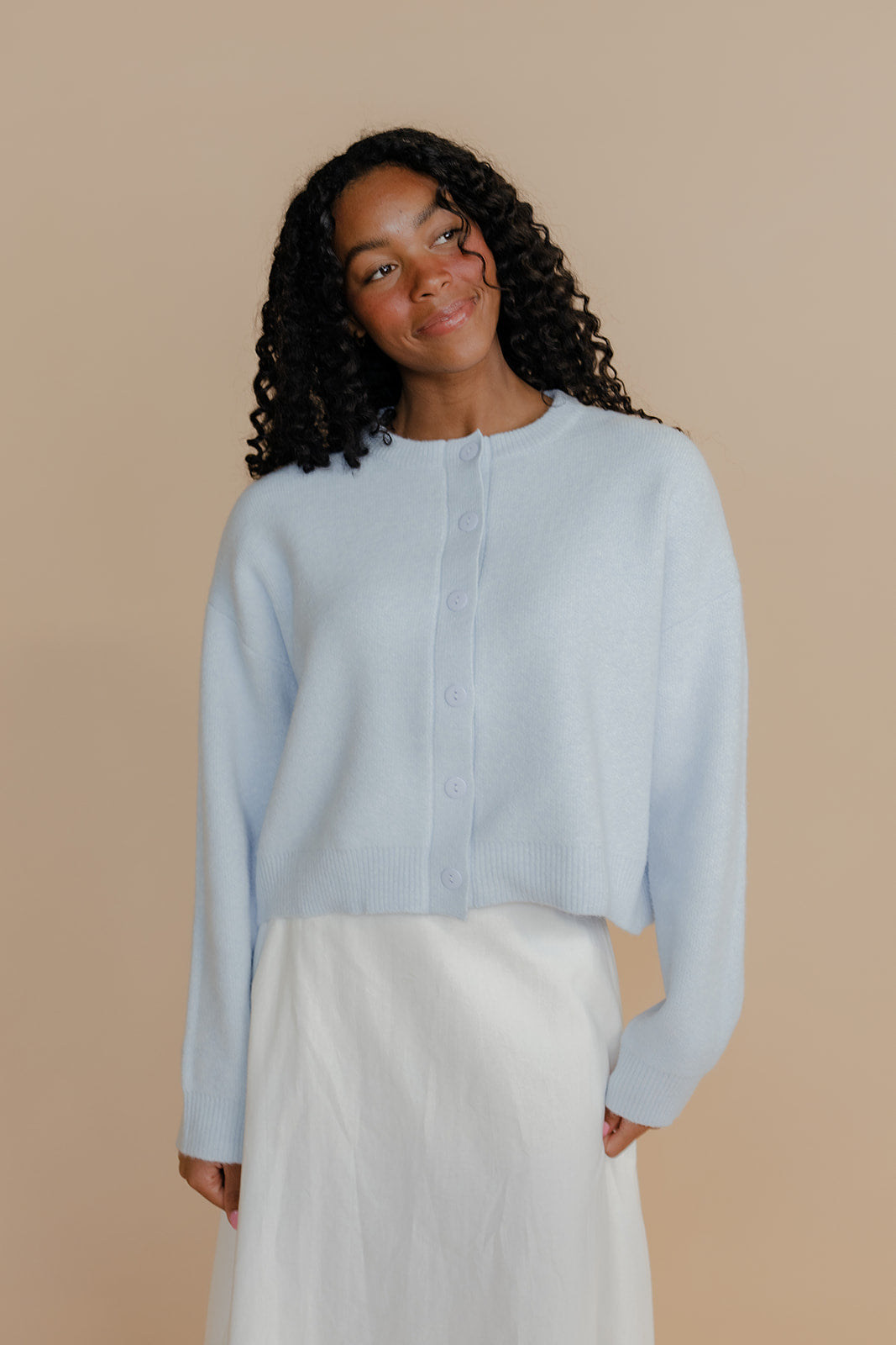 Woman wearing a light blue shirt and white pants against a beige background