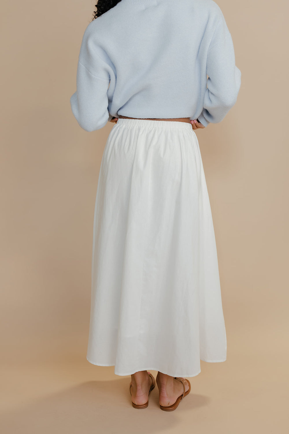 Person wearing a light blue sweater and white skirt on a beige background