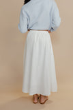 Person wearing a light blue sweater and white skirt on a beige background