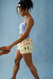 Woman wearing a light blue sports bra and patterned shorts against a solid background