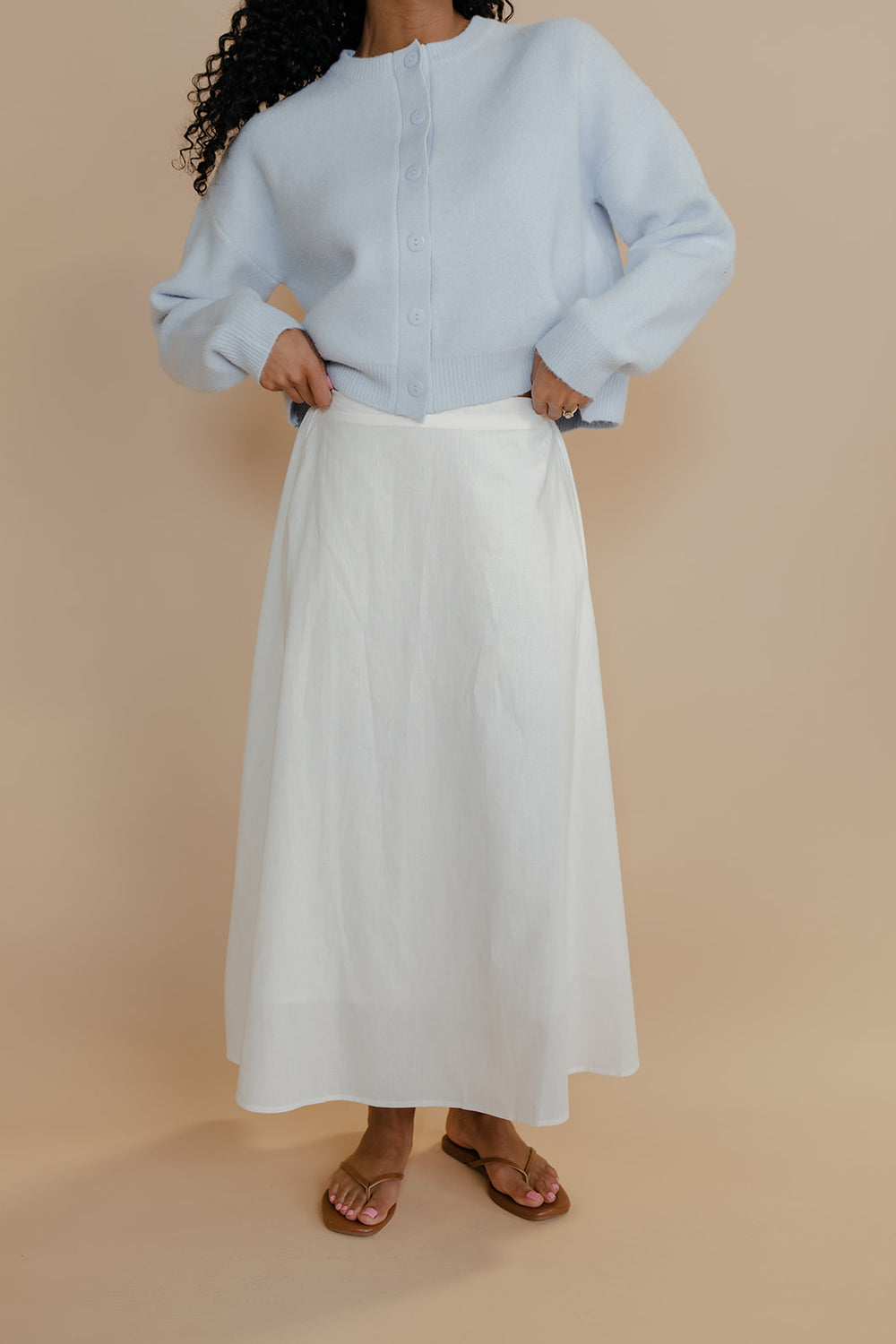 Person wearing a light blue sweater and white skirt on a beige background