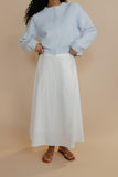Person wearing a light blue sweater and white skirt on a beige background