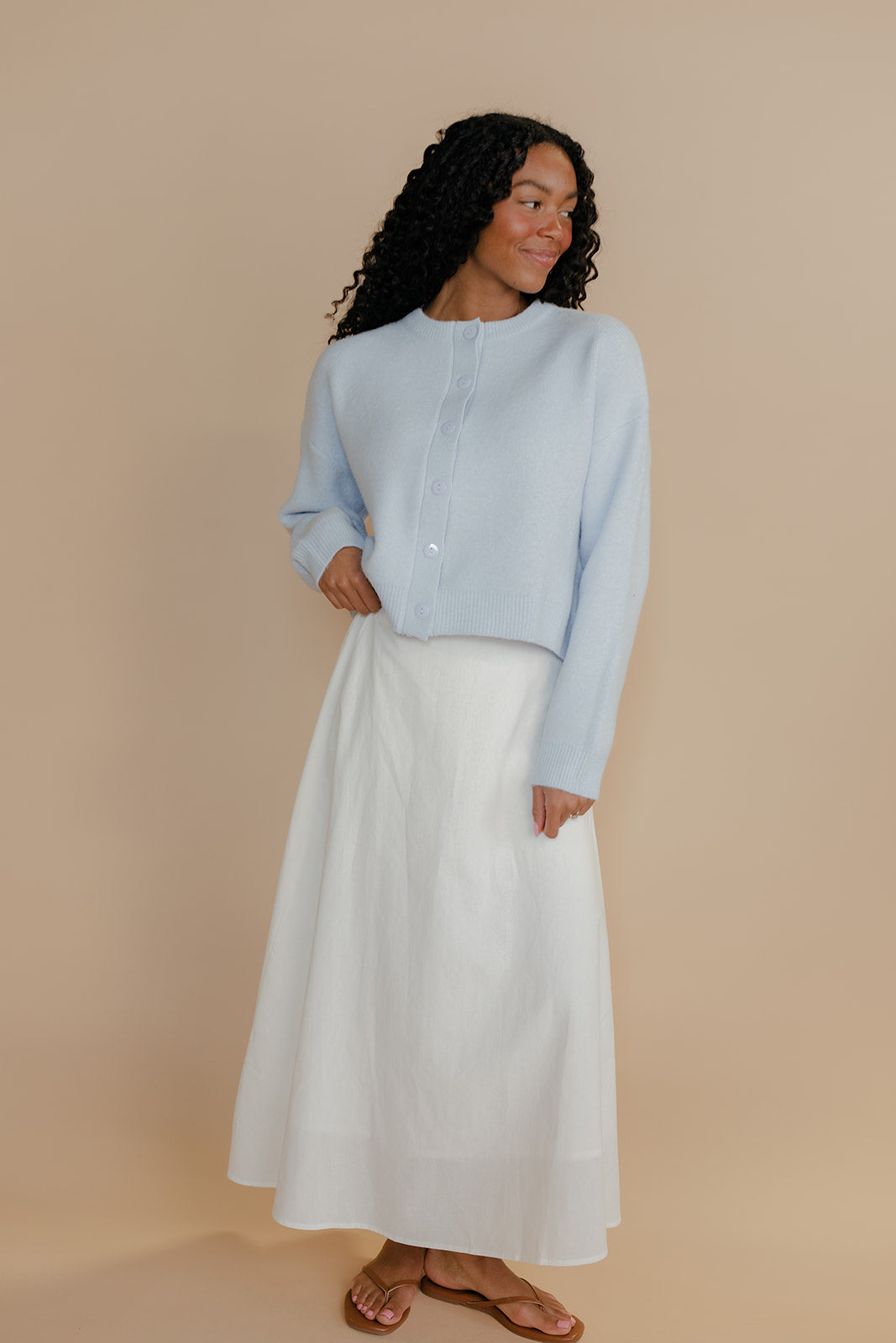 Woman wearing a light blue top and white skirt against a beige background