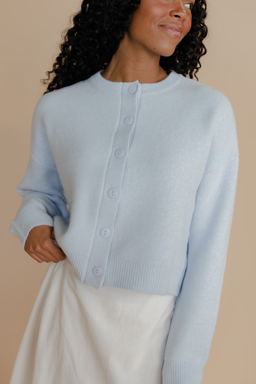 Woman wearing a light blue cardigan against a beige background