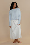 Woman wearing a light blue top and white skirt on a beige background