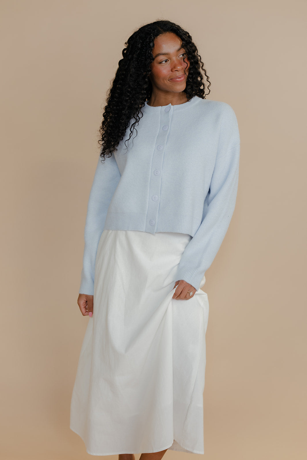 Woman wearing a light blue shirt and white skirt against a beige background